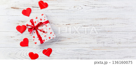 Valentine or other holiday handmade present in paper with red hearts and gifts box in holiday wrapper. Present box of gift on white wooden table top view with copy space, empty space for design 136160075