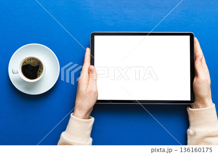 Close up image woman hands holding digital tablet with blank copy space screen for your text message or promotional content om table with cup of coffee. hands of a woman holding blank tablet device 136160175