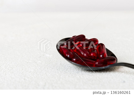 Vitamin capsules in a spoon on a colored background. Pills served as a healthy meal. Red soft gel vitamin supplement capsules on spoon 136160261