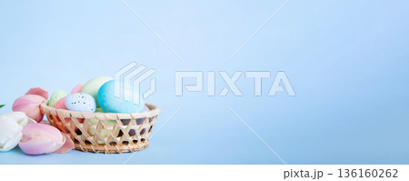 Happy Easter composition. Easter eggs in basket on colored table with yellow Tulips. Natural dyed colorful eggs background with copy space 136160262