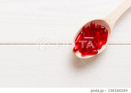 Vitamin capsules in a spoon on a colored background. Pills served as a healthy meal. Red soft gel vitamin supplement capsules on spoon Vitamin capsules in a spoon on a colored background. Pills served as a healthy meal. Red soft gel vitamin supplement capsules on spoon 136160264