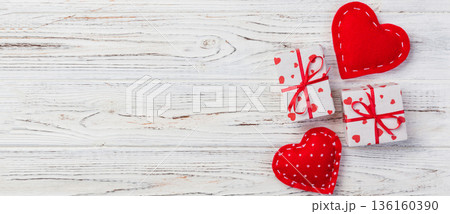 Valentine or other holiday handmade present in paper with red hearts and gifts box in holiday wrapper. Present box of gift on white wooden table top view with copy space, empty space for design 136160390