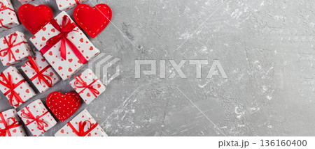 Valentine or other holiday handmade present in paper with red hearts and gifts box in holiday wrapper. Present box of gift on grey cement table top view with copy space, empty space for design 136160400