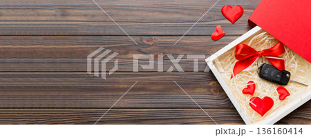 Black car key in a present box with a ribbon and red heart on colored background. Valentine day composition Top view 136160414