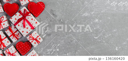 Valentine or other holiday handmade present in paper with red hearts and gifts box in holiday wrapper. Present box of gift on grey cement table top view with copy space, empty space for design 136160420