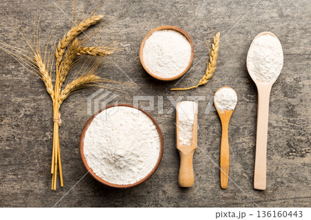 Flat lay of Wheat flour in wooden bowl with wheat spikelets on colored background. world wheat crisis Flat lay of Wheat flour in wooden bowl with wheat spikelets on colored background. world wheat crisis 136160443