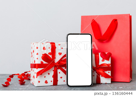 mobile phone with blank screen on colored background with hearts, calendar and gift box, valentine day concept perspertive view flat lay mobile phone with blank screen on colored background with hearts, calendar and gift box, valentine day concept perspertive view flat lay 136160444