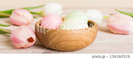 Happy Easter composition. Easter eggs in basket on colored table with yellow Tulips. Natural dyed colorful eggs background with copy space 136160529