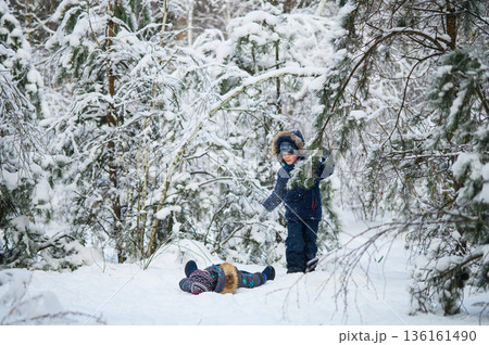 Two young children enjoying active winter day outdoors in snowy forest. Kids play, explore nature, ride a sled, and have fun among snow-covered trees. Two young children enjoying active winter day outdoors in snowy forest. Kids play, explore nature, ride a sled, and have fun among snow-covered trees. 136161490