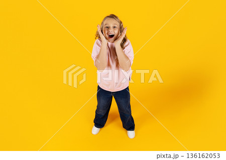 Excited preteen girl reacting with surprise and joy, standing on yellow background 136162053