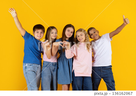 Preteen children smiling and making friendly gestures on bright yellow background 136162067