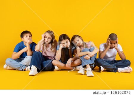 Bored children sitting on floor looking sad and tired on yellow background Bored children sitting on floor looking sad and tired on yellow background 136162073
