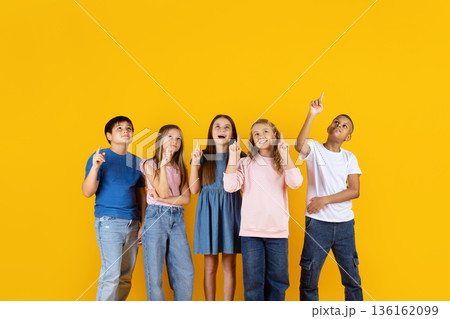 Preteen children looking up and pointing on yellow background, expressing curiosity Preteen children looking up and pointing on yellow background, expressing curiosity 136162099