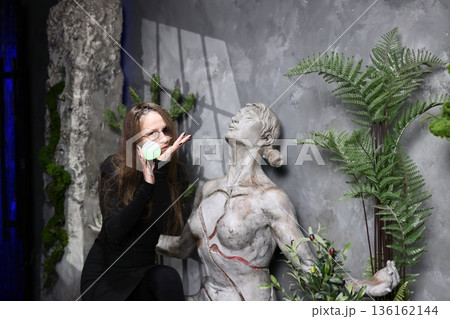 Woman carefully arranging greenery around statue during sunset ambiance 136162144
