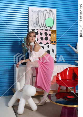 Individual dressed in pink skirt sitting on white sofa against blue wall 136162145