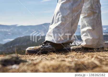 Man standing with snow covered boots and pants on dry grass outdoors. Hiking and winter outdoor activity concept for adventurer. Man standing with snow covered boots and pants on dry grass outdoors. Hiking and winter outdoor activity concept for adventurer. 136162162