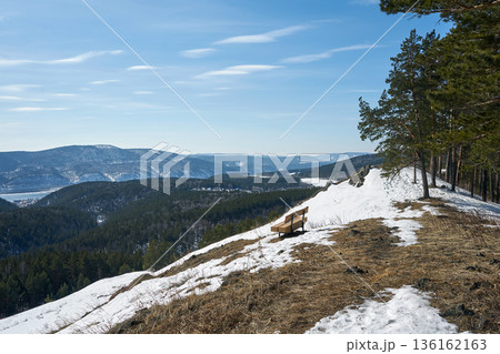 Empty wooden bench on a snowy hill overlooking a winter forest valley. Beautiful landscape for travel and nature exploration. Empty wooden bench on a snowy hill overlooking a winter forest valley. Beautiful landscape for travel and nature exploration. 136162163