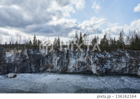 Frozen marble quarry in Ruskeala Mountain Park with evergreen forest on cliff top. Winter landscape for travel and nature concept. Frozen marble quarry in Ruskeala Mountain Park with evergreen forest on cliff top. Winter landscape for travel and nature concept. 136162164