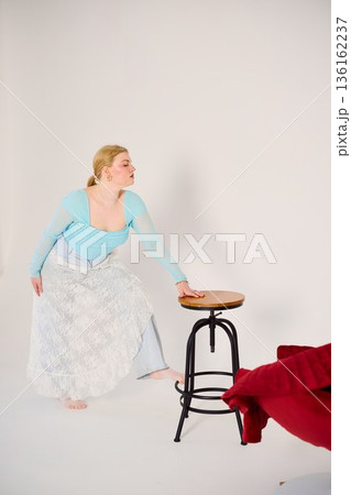 Woman stylist reaching for stool during studio shoot Woman stylist reaching for stool during studio shoot 136162237