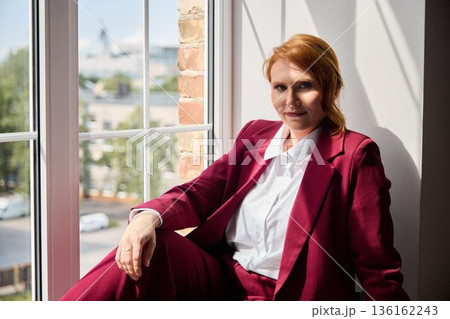 Stylish woman in burgundy suit looks over urban cityscape 136162243