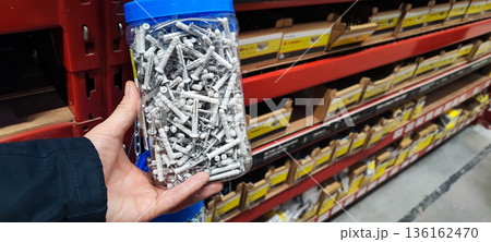 A man's hand picking up a handful of metal nails from a cardboard box at a hardware store or warehouse. Concept art of handicrafts, building materials, craftsmanship, and industrial supplies. 136162470