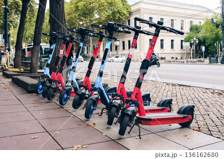 Electric scooters parked along the sidewalk in a busy urban area during the day Electric scooters parked along the sidewalk in a busy urban area during the day 136162680