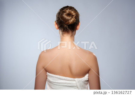 Woman stands with back turned, towel wrapped, in simple indoor setting with plain background Woman stands with back turned, towel wrapped, in simple indoor setting with plain background 136162727