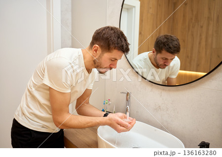Man standing in bathroom and washing hands under running water at sink Man standing in bathroom and washing hands under running water at sink 136163280