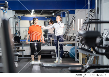 Woman receiving personal trainer guidance for weightlifting workout Woman receiving personal trainer guidance for weightlifting workout 136163693