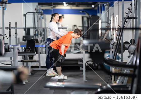 Personal trainer assisting woman with resistance training in gym 136163697