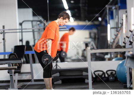 Senior woman performing strength training with barbell in gym 136163703