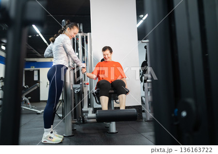 Personal trainer guiding senior woman doing leg exercise 136163722