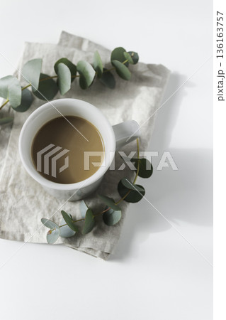俯瞰のコーヒーカップとユーカリ リネンの上のミニマルな白背景 俯瞰のコーヒーカップとユーカリ リネンの上のミニマルな白背景 136163757