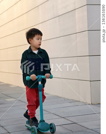Young Child Riding A Scooter Down A Sleek, Modern Walkway. Young Child Riding A Scooter Down A Sleek, Modern Walkway. 136163890