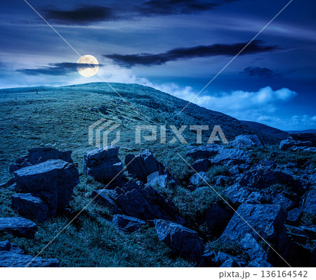 mountain landscape in summer under dark sky at night. lush green grass and sharp rocks on steep hillside in full moon light. beautiful view of remote place in mysterious alpine environment for fantasy 136164542