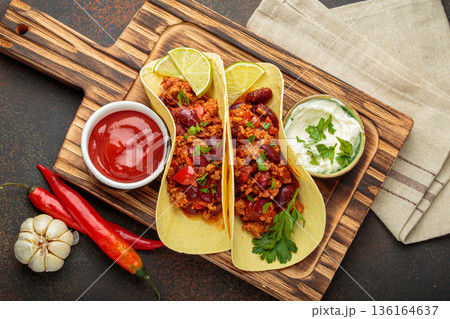 Mexican chili con carne tacos with lime, ketchup, sour cream and fresh herbs on wooden board top view 136164637
