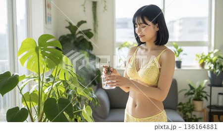 観葉植物の手入れをして微笑む黄色い下着姿の日本人女性 136164881