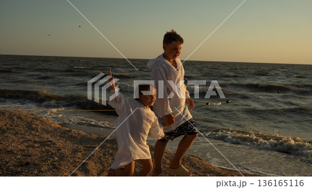 Children create happy childhood memories during sunset on the seashore A brother and sister stroll along the sunny beach, where the ocean waves gently crash, holding hands and enjoying the fresh air. Children create happy childhood memories during sunset on the seashore A brother and sister stroll along the sunny beach, where the ocean waves gently crash, holding hands and enjoying the fresh air. 136165116