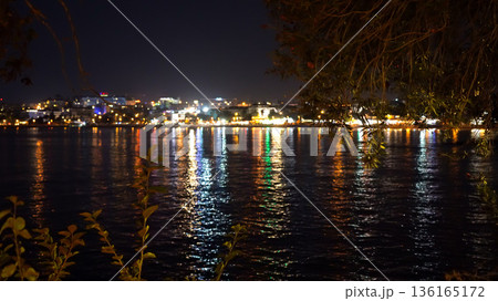 A Serene Night View of City Lights Reflecting on Calm Water Surrounded by Nature's Beauty and a Tranquil Atmosphere 136165172