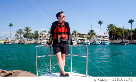 Relaxing on a Boat in Sunny Waters with Palm Trees in the Background and a Safe Life Jacket for Enjoying the Scenic Views Relaxing on a Boat in Sunny Waters with Palm Trees in the Background and a Safe Life Jacket for Enjoying the Scenic Views 136165173