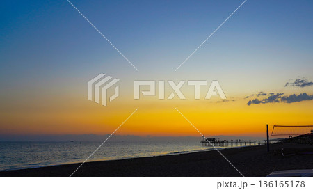 A Serene Evening at the Beach: Captivating Colors of Sunset Reflecting on the Calm Ocean with a Pier in the Distance 136165178