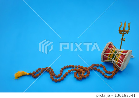 Maha Shivratri. Hindu damru, trishula, and rudraksha mala on blue background Maha Shivratri. Hindu damru, trishula, and rudraksha mala on blue background 136165341