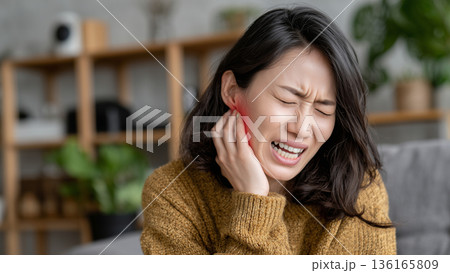 室内で頬に手を当て歯痛や知覚過敏の痛みを感じる女性 136165809