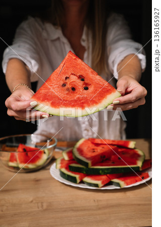 Woman holds a slice of watermelon in a cozy kitchen setting during summer 136165927