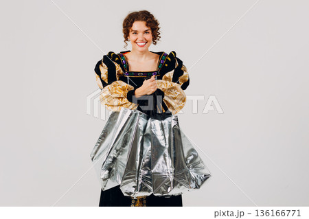 Young adult smiling woman dressed in a medieval dress holding shopping bags in hands isolated white background 136166771