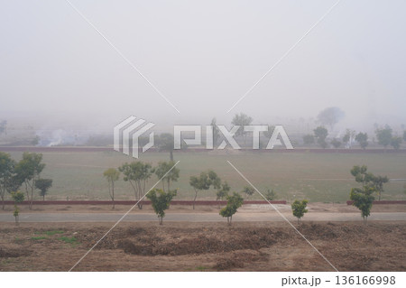 Air pollution and smog. Gray smoke from bonfires hangs over the suburbs. Traditional fire-raising or burning of turf, sod and dry grass on land plots and fields in Punjab, South Asia. Air pollution and smog. Gray smoke from bonfires hangs over the suburbs. Traditional fire-raising or burning of turf, sod and dry grass on land plots and fields in Punjab, South Asia. 136166998