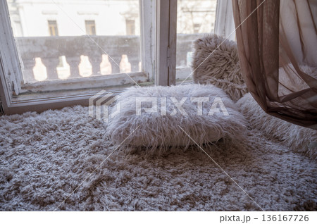 A cozy faux fur blanket and pillows on the windowsill of a large window A cozy faux fur blanket and pillows on the windowsill of a large window 136167726