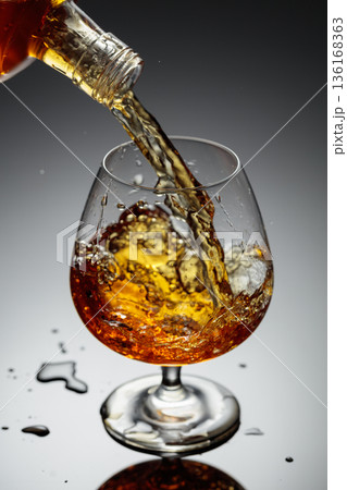 The amber-gold strong alcoholic beverage is poured into a glass. The amber-gold strong alcoholic beverage is poured into a glass. 136168363