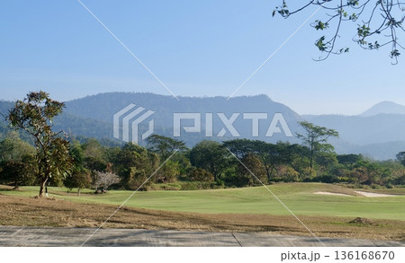 A picturesque golf course scene featuring vibrant green fairways and sand traps, with a lush forest and hazy distant mountains under a clear blue sky, evoking tranquility and outdoor sport. A picturesque golf course scene featuring vibrant green fairways and sand traps, with a lush forest and hazy distant mountains under a clear blue sky, evoking tranquility and outdoor sport. 136168670