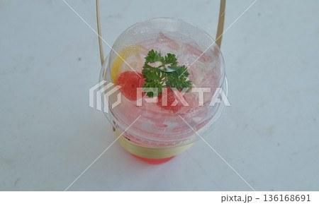 Vibrant pink iced soda garnished with fresh lemon slice, maraschino cherries, and green parsley in a plastic cup, isolated on a light background for summer. 136168691